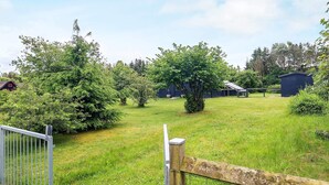 Een omheind terrein met gazon, bomen en een gebouw met schuine dak.