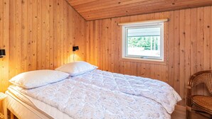 Een slaapkamer met houten lambrisering, een bed, een raam en een stoel.