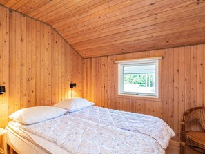 Quarto com painéis de madeira, uma cama, uma janela e uma cadeira.