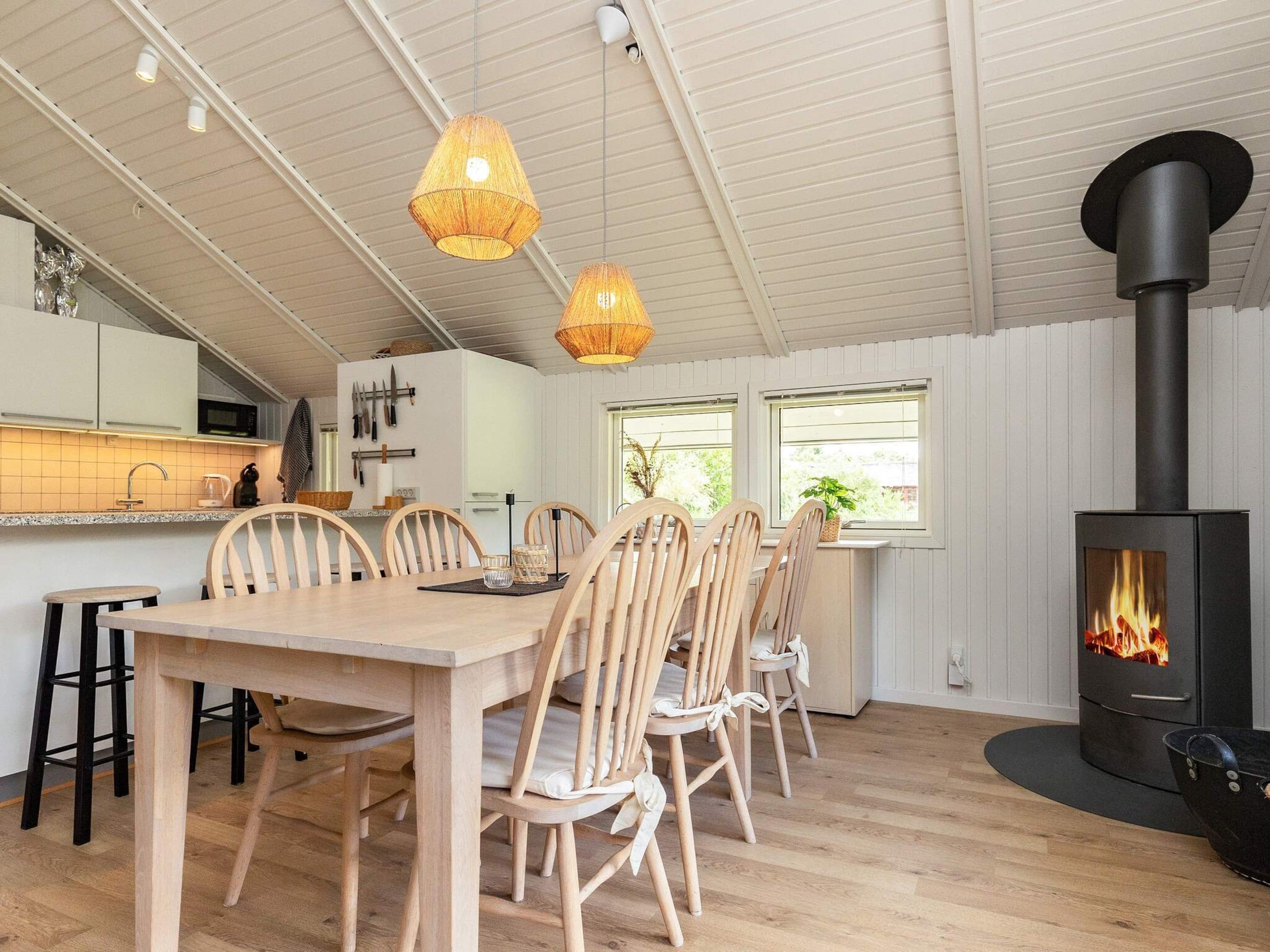 A modern kitchen with white cabinets, a dining area with wooden chairs, and a wood-burning stove.
