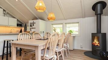 A modern kitchen with white cabinets, a dining area with wooden chairs, and a wood-burning stove.