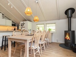 Et moderne køkken med hvide skabe, et spiseområde med træstole og en brændeovn.