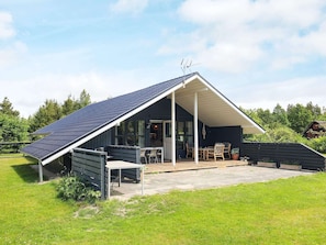 A modern house with a sloped roof, a covered patio with outdoor furniture, and a large window. - 8 Person Holiday Home in Hojslev (Hojslev)