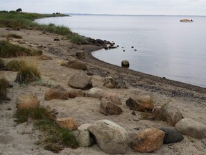A coastal landscape with a sandy beach, scattered rocks, and a calm sea.