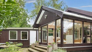 Ett modernt hus med stora glasfönster, en träveranda och utomhusmöbler.