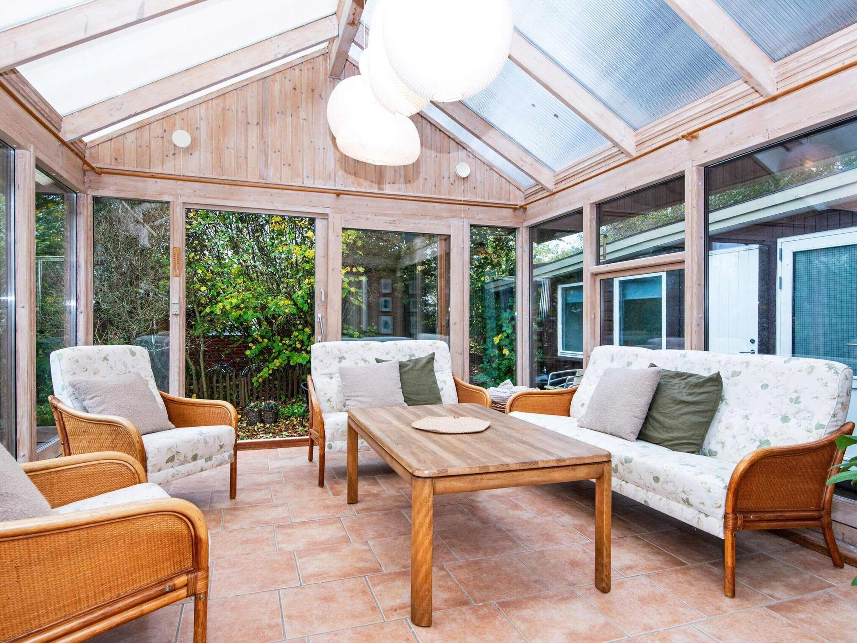 A sunroom with wicker furniture, large windows, and a wooden table.