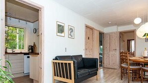 Ett modernt kök med en inbyggd diskmaskin, en matplats med ett träbord och stolar samt ett vardagsrum med en svart lädersoffa och en trästol.