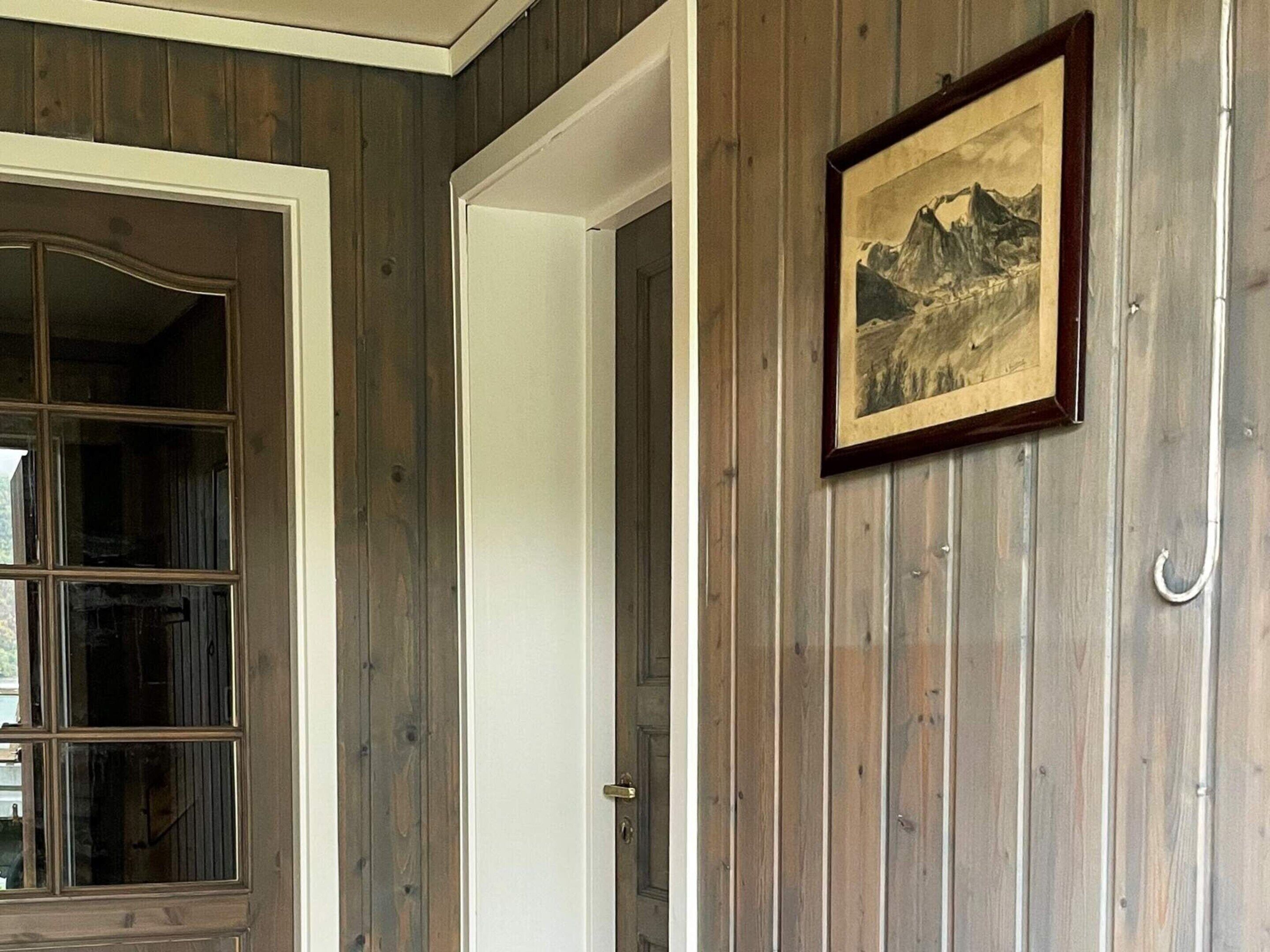 Ein Zimmer mit Holzwänden, einem gerahmten Bild an der Wand und einer Tür mit weißem Rahmen.