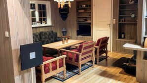 A cozy room with a wooden floor, a dining table with chairs, a TV, and a bookshelf.