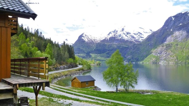 A wooden cabin with a deck overlooking a lake and mountains.