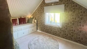 A bedroom with a sloped ceiling, a bed with pillows, a window with a view, and an air conditioning unit.