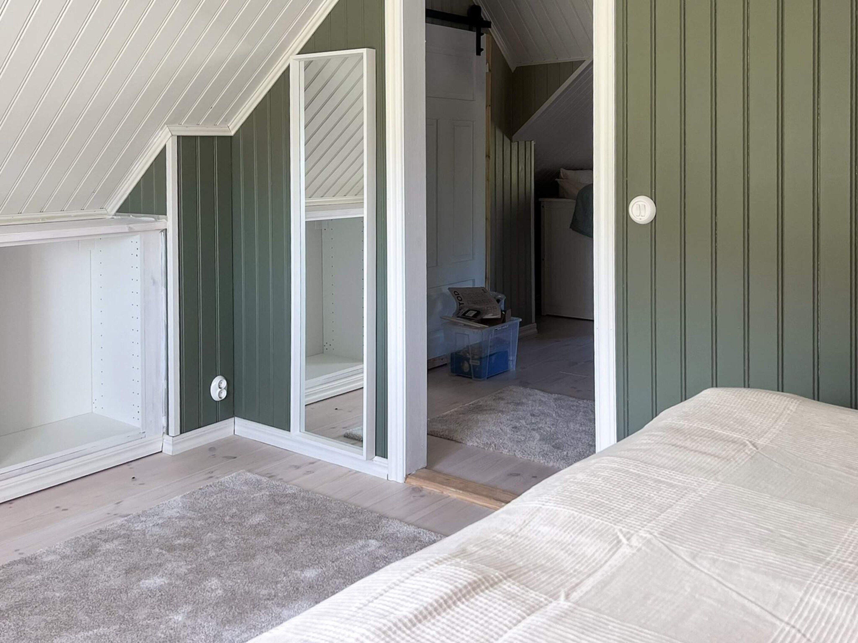 A room with a sloped ceiling, a bed, a closet, and a hallway leading to a staircase.