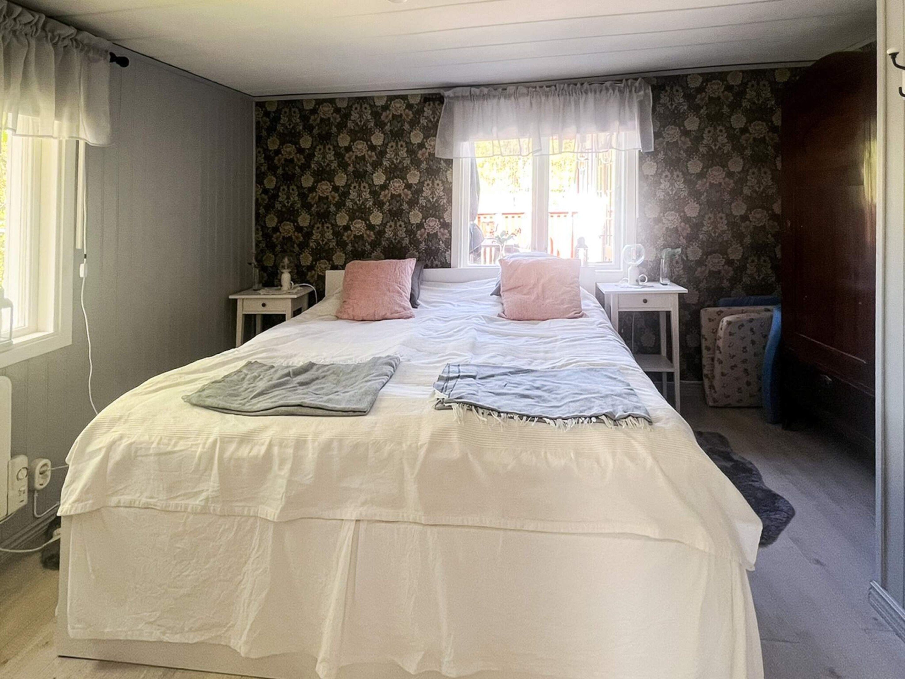 Un dormitorio con una cama grande, dos mesitas de noche, un ventanal con cortinas y un papel tapiz floral.