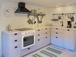 A modern kitchen with white cabinetry, a stove, a black range hood, and various kitchen utensils hanging on the wall. - 5 Person Holiday Home in Haradsback (Ryd)