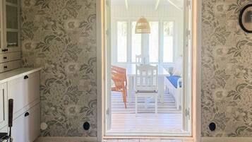 A room with a patterned wallpaper, a wooden floor, a white door leading to an outdoor area with a table and chairs, and a hanging light fixture.
