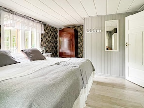 A bedroom with a bed, a nightstand, a wooden wardrobe, a mirror, and a window with curtains. - 5 Person Holiday Home in Haradsback (Ryd)