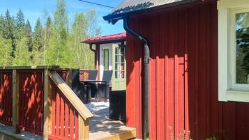 A red wooden building with a deck, a window, and a door.