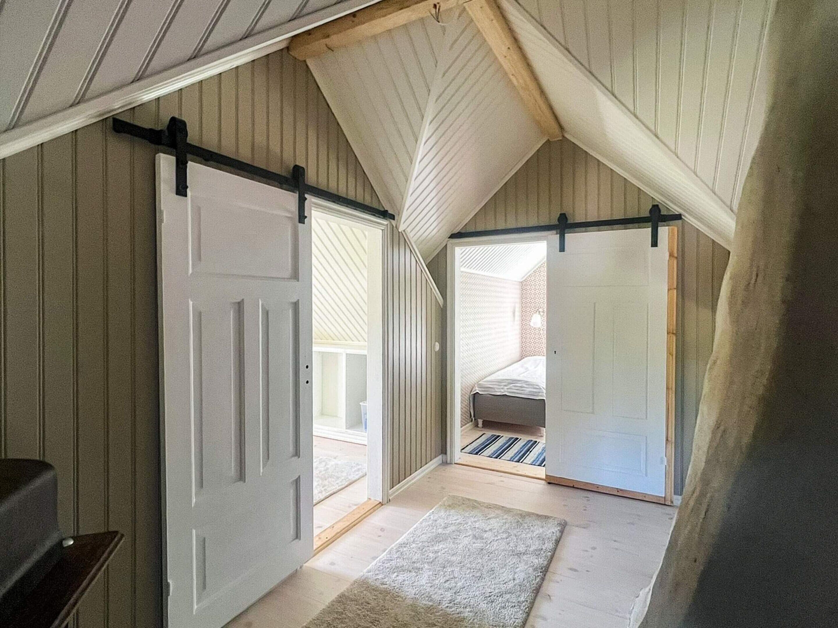 A loft bedroom with a sloped ceiling, a bed, a sliding door, and a small rug.