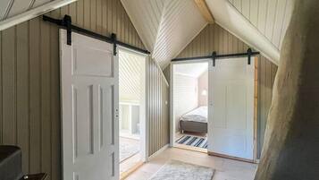 A loft bedroom with a sloped ceiling, a bed, a sliding door, and a small rug.