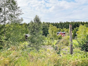 A rural landscape with a red house surrounded by dense forest and greenery. - 5 Person Holiday Home in Haradsback (Ryd)