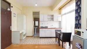 A compact kitchen with white cabinets, a dining table with chairs, a microwave, and a refrigerator. - Cool Luxurious Studios (Nairobi)