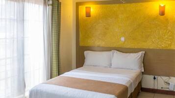 A hotel room with a bed, a window with curtains, and a wall with two wall sconces.