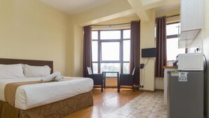 A hotel room with a bed, a desk, a chair, a window, and a refrigerator. - Cool Luxurious Studios (Nairobi)