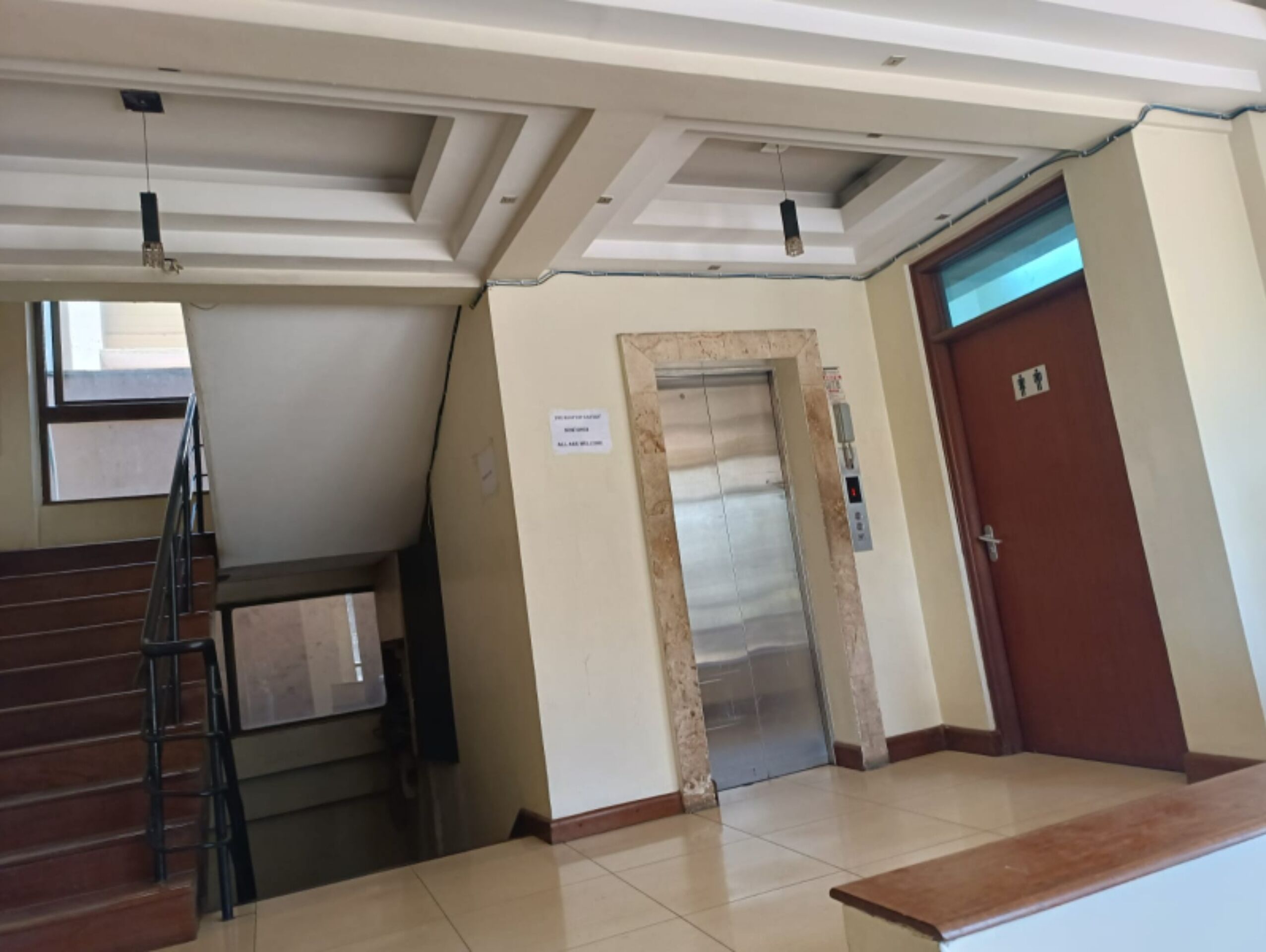 A hotel lobby with a staircase, an elevator, and a reception desk.