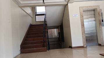 A staircase with a handrail leading to a landing, an elevator, and a tiled floor.