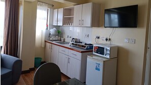 A compact kitchen with white cabinets, a microwave, a sink, and a flat-screen TV mounted on the wall. - Cool Luxurious Studios (Nairobi)
