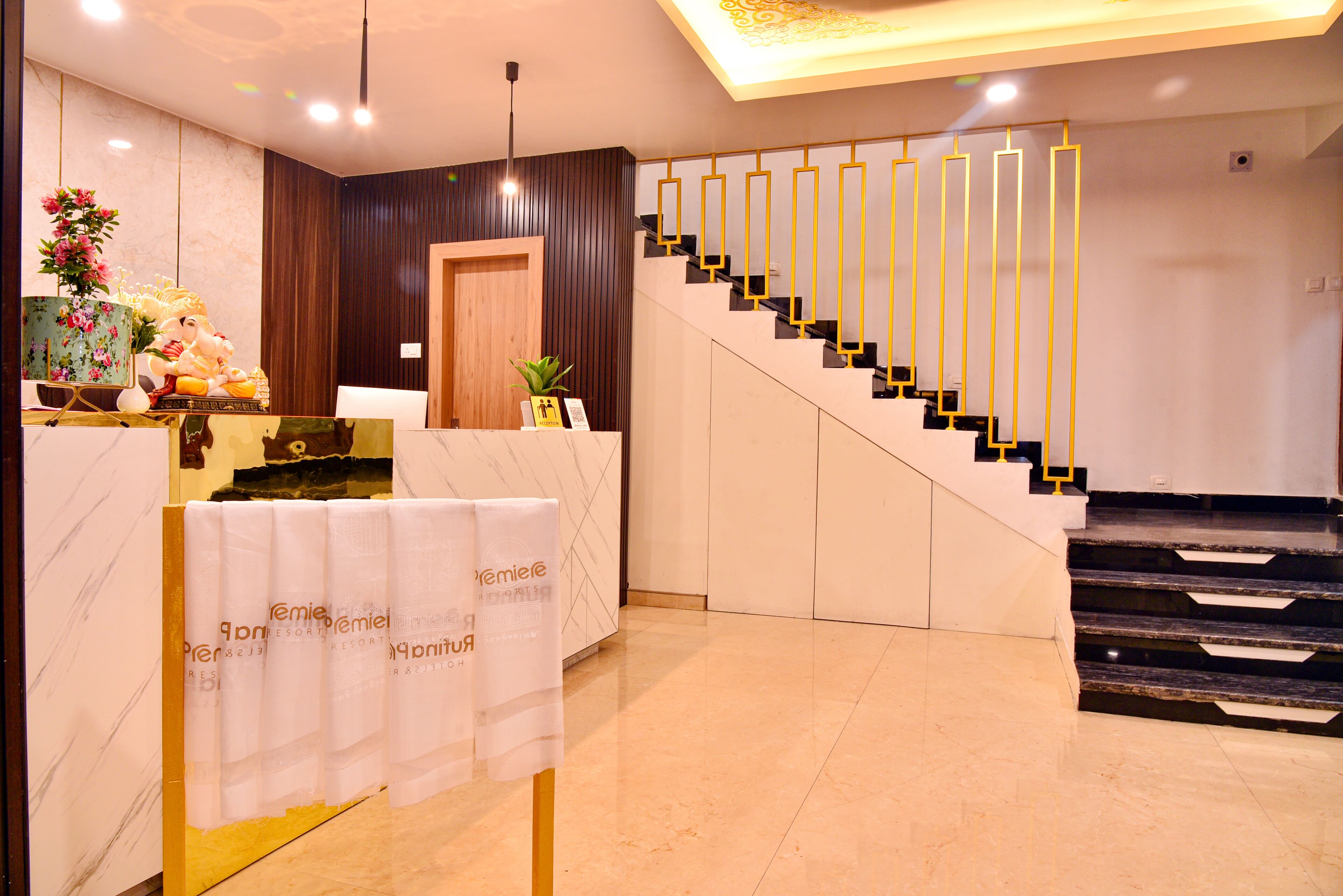 A hotel reception area with a marble counter, a staircase with golden railings, and a wooden door.