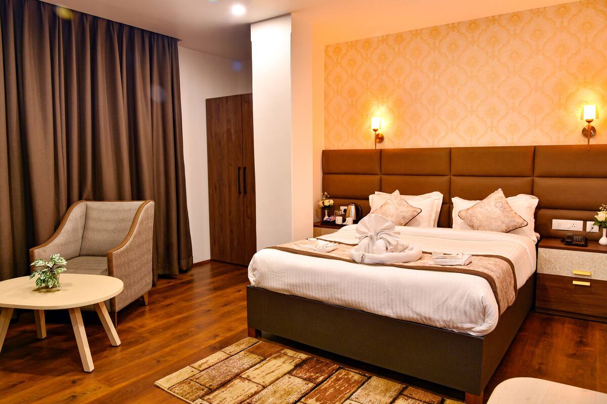 A hotel room with a large bed, a chair, a small table, and a nightstand.
