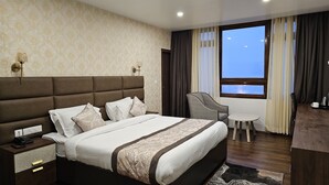 A hotel room with a large bed, a desk, a chair, and a view of the sky through the window. - Rufina Pinasa Residency (Gangtok)