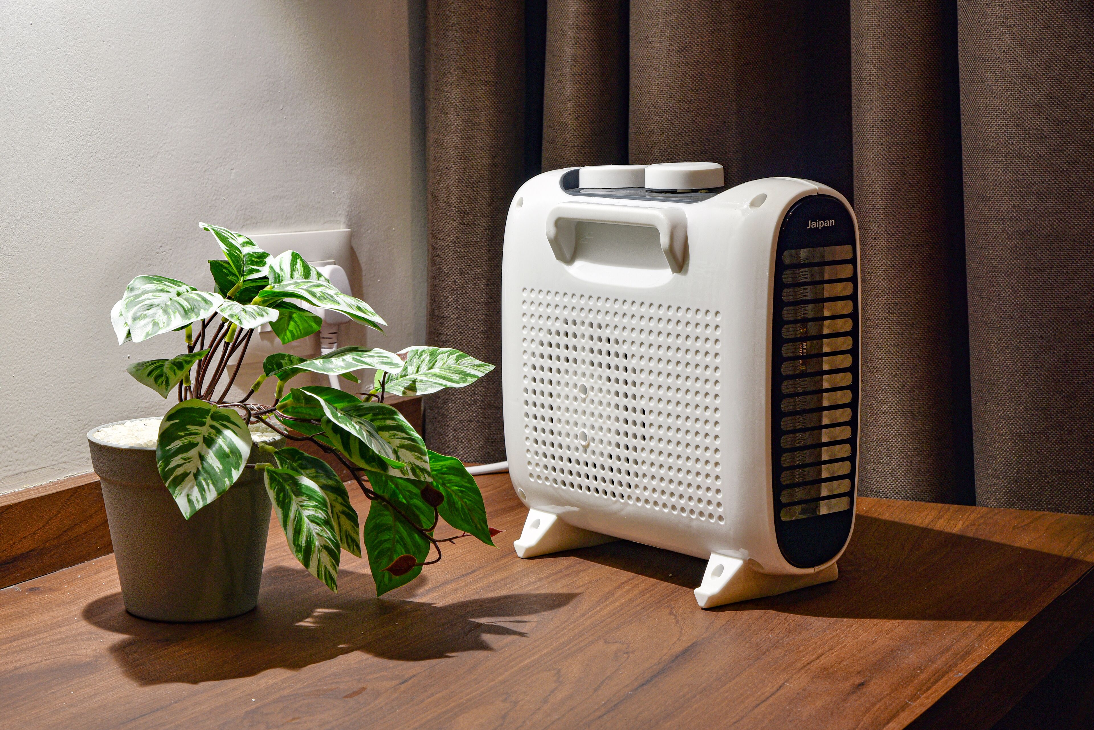 A white portable heater with a control panel on a wooden surface next to a potted plant.