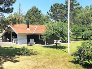 Una casa pequeña con techo rojo, garaje y un patio con una silla y una mesa.