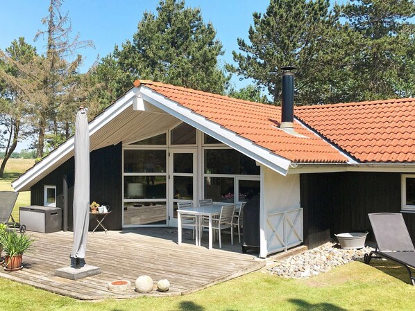 A house with a sloped roof, large windows, a deck, outdoor furniture, and a chimney.