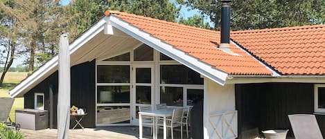 A modern house with a sloped roof, large windows, a deck with outdoor furniture, and a chimney.