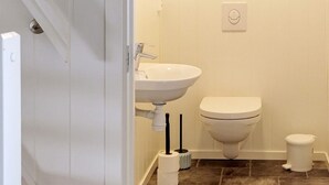 A bathroom with a white sink, toilet, and bidet, with brown tiled flooring.