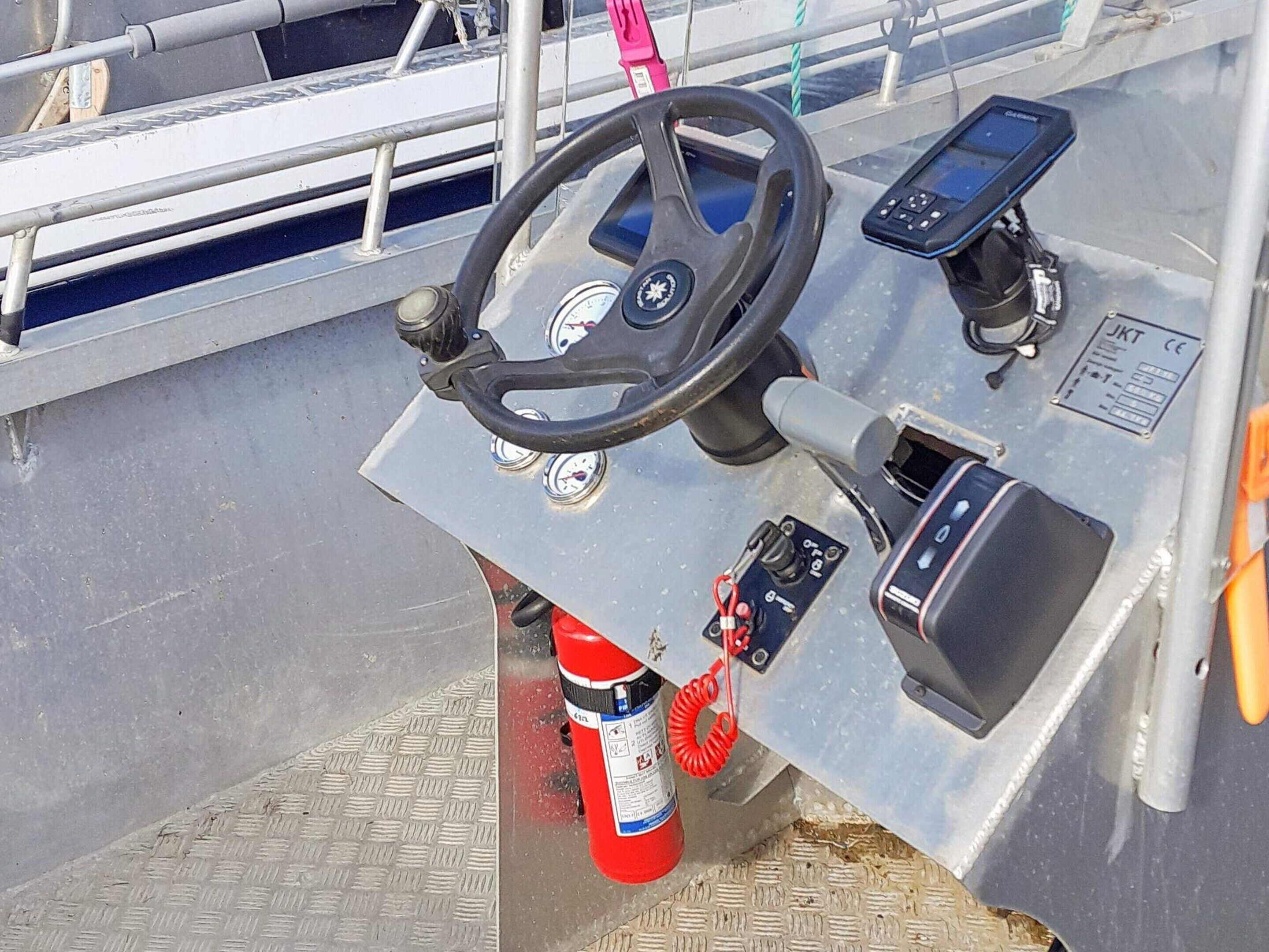 A boat's control station with a steering wheel, a control panel, and a fire extinguisher.