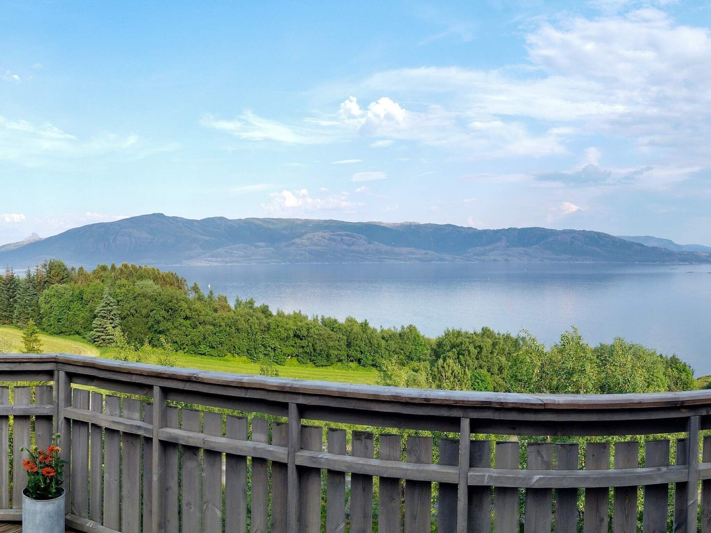 A view of a lake with mountains in the background, a wooden deck, and a metal railing.