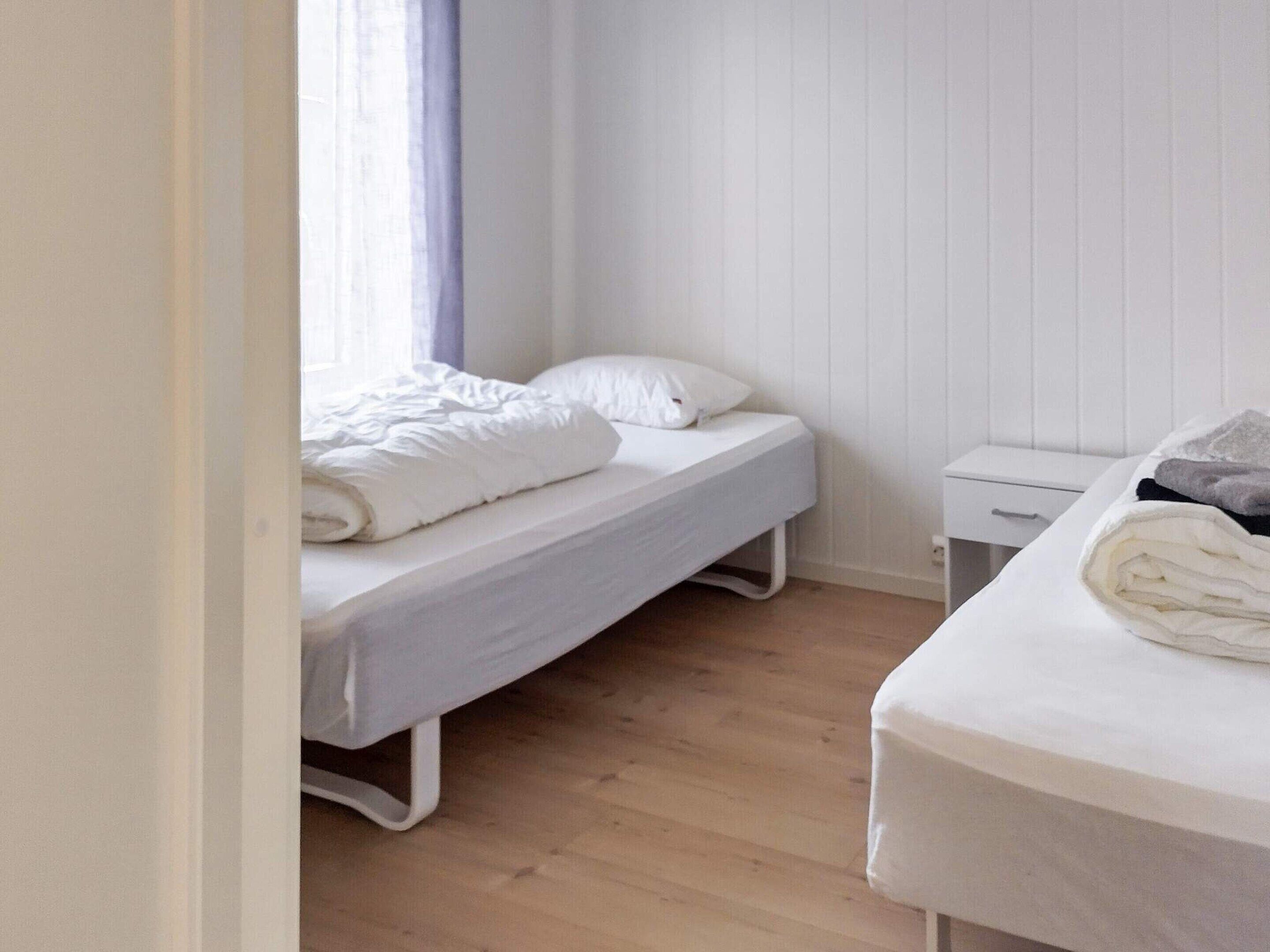 Un dormitorio pequeño y ordenado con una cama individual, una mesita de noche y una ventana con cortinas.