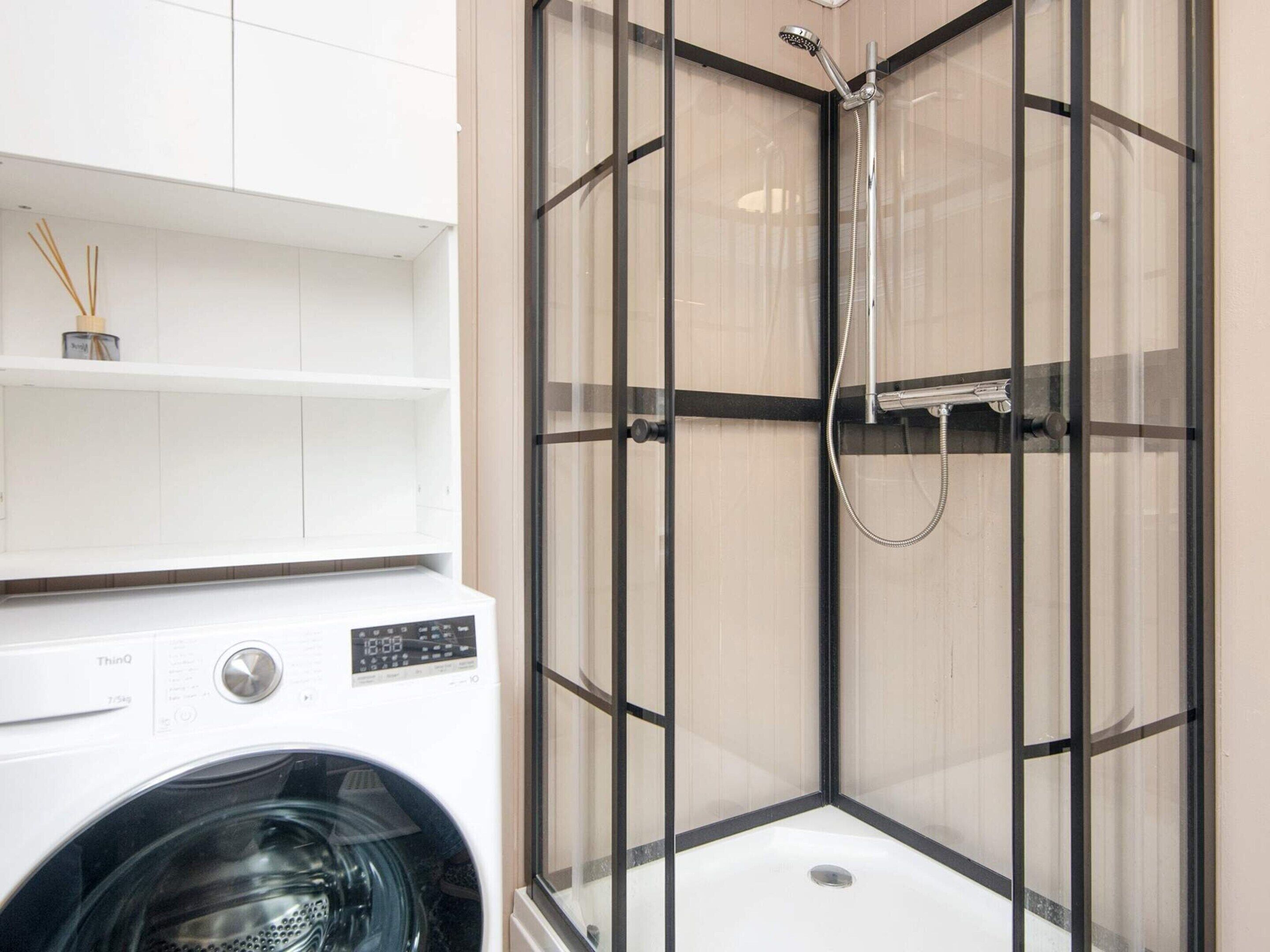 A modern bathroom with a built-in shower, a washing machine, and a shelf with toiletries.