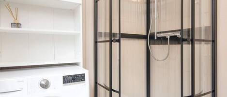 A modern bathroom with a built-in shower, a washing machine, and a shelf with toiletries.