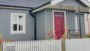 Een huis met een grijze gevel, een rode deur en een witte schutting.