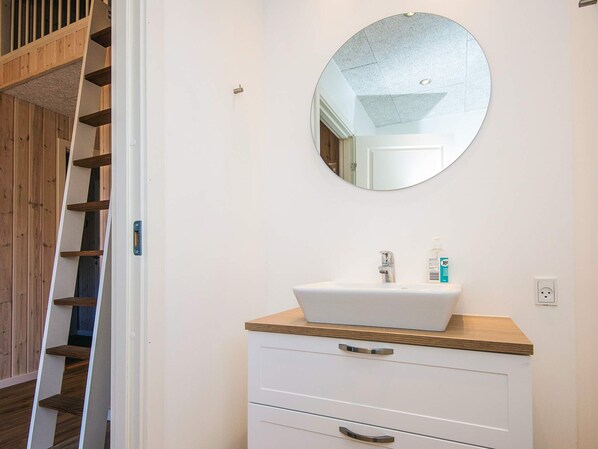 A bathroom with a white sink, wooden countertop, and a round mirror.