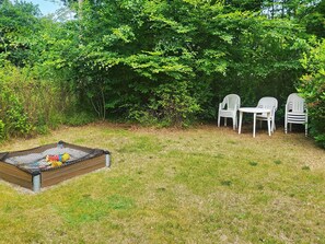 A grassy outdoor area with a small play area, including a netted playpen and a table with chairs.
