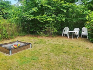 A grassy outdoor area with a play structure and three white plastic chairs.