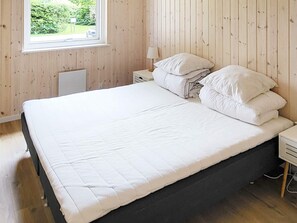 A bedroom with a large bed, a bedside table, a lamp, and a window with a view of greenery.