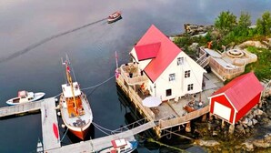 Un bateau amarré, avec une maison dotée de toits rouges et d’un petit abri de jardin.