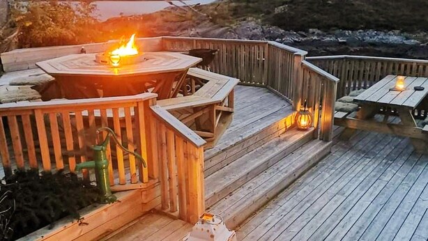 Une terrasse en bois avec un foyer et des lanternes, entourée d’une balustrade en bois.